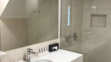 Un baño moderno con un lavamanos blanco, un espejo grande y una ducha con cerramiento de vidrio.