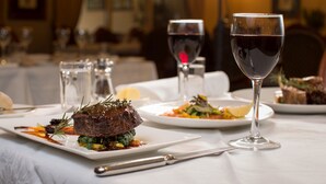 A dining table with plates of food, a wine glass, and cutlery. - Canterbury International Hotel (Forest Hill)