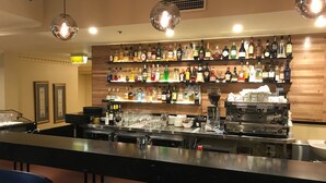 A bar area with a long counter, multiple shelves of liquor bottles, and a coffee machine. - Canterbury International Hotel (Forest Hill)