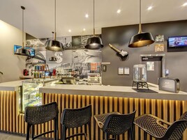 A modern bar area with a counter, black chairs, and a guitar on the wall.