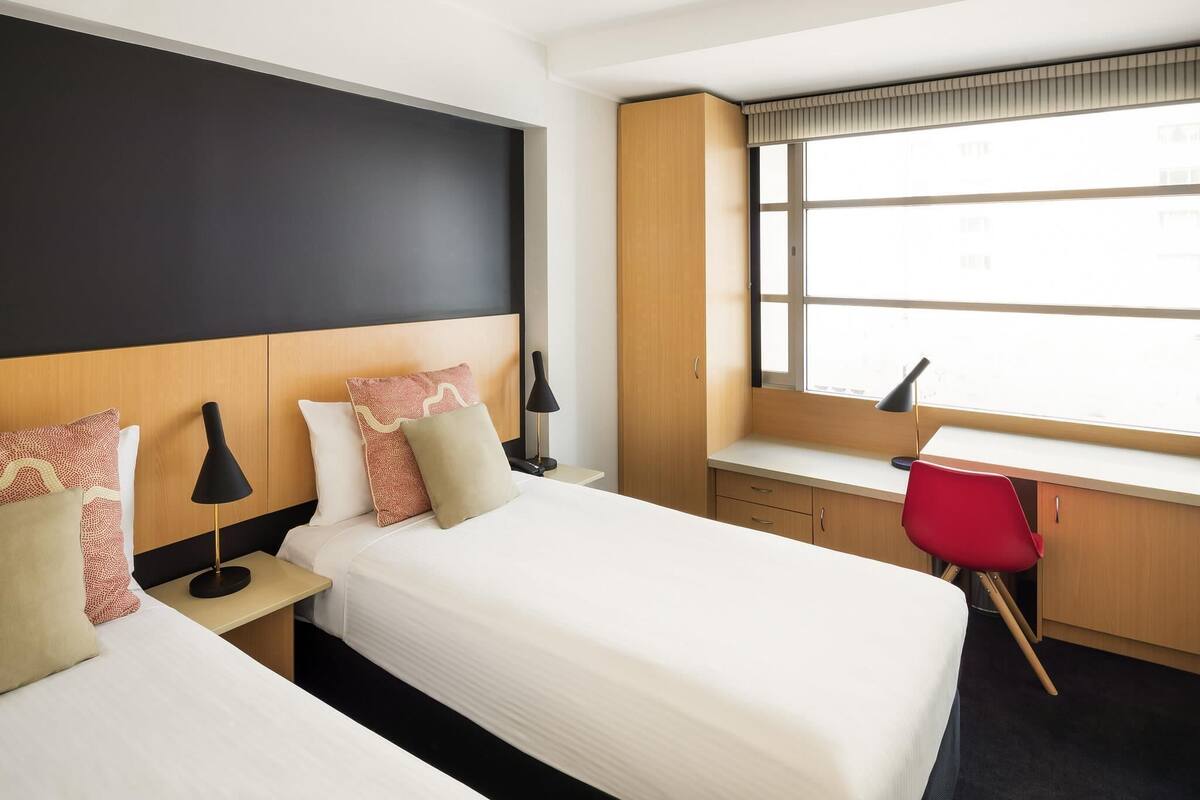 Una habitación de hotel con dos camas, un escritorio y una ventana.