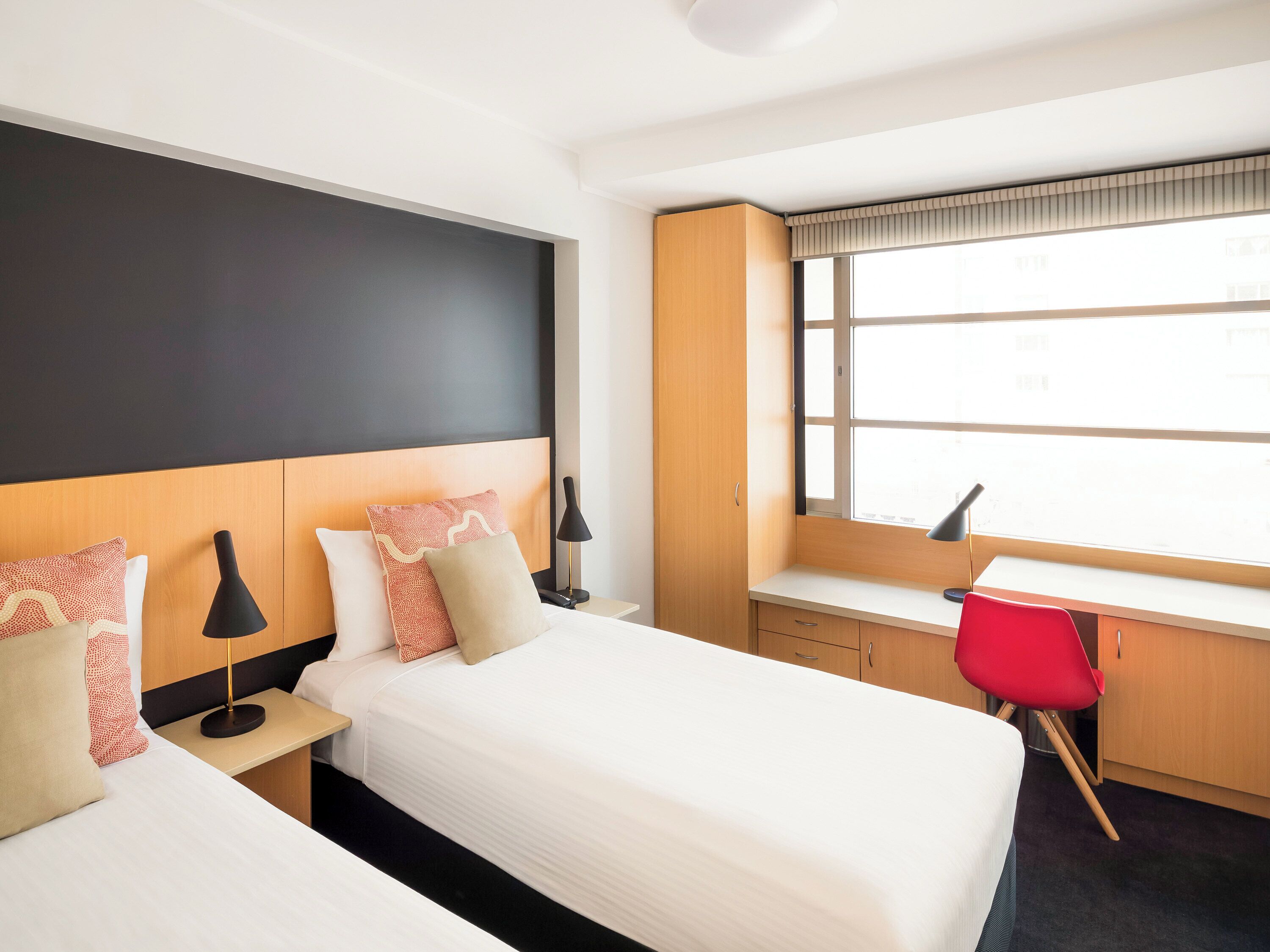 A hotel room with a bed, bedside tables, a desk, a chair, and a window.