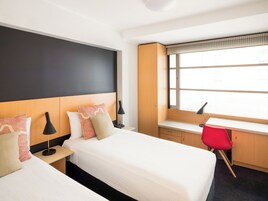 A hotel room with a bed, bedside tables, a desk, a chair, and a window.