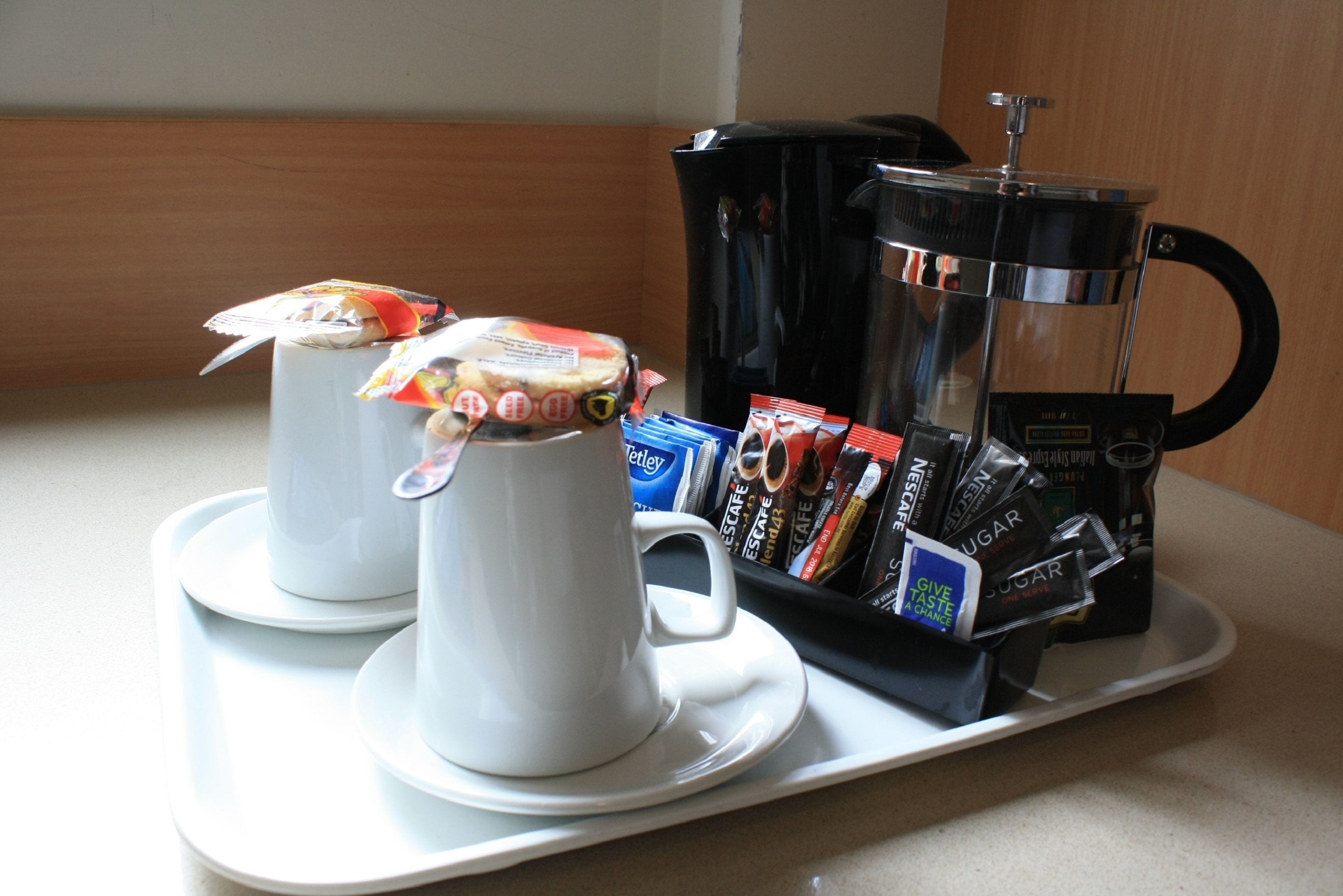 Una bandeja con dos tazas blancas, una cafetera y varios pods de café.