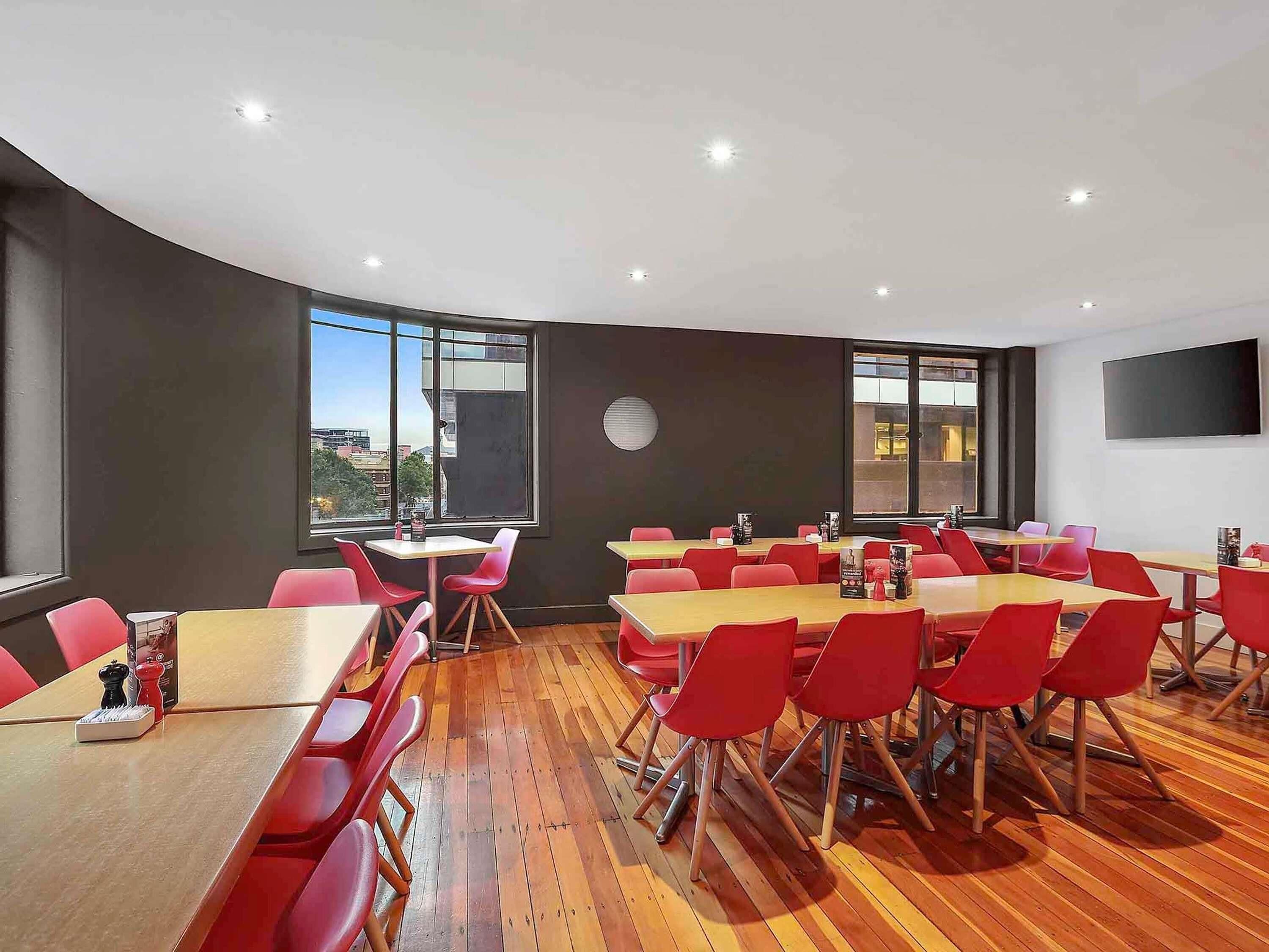 A conference room with tables and chairs, large windows, a flat-screen TV, and a wooden floor.