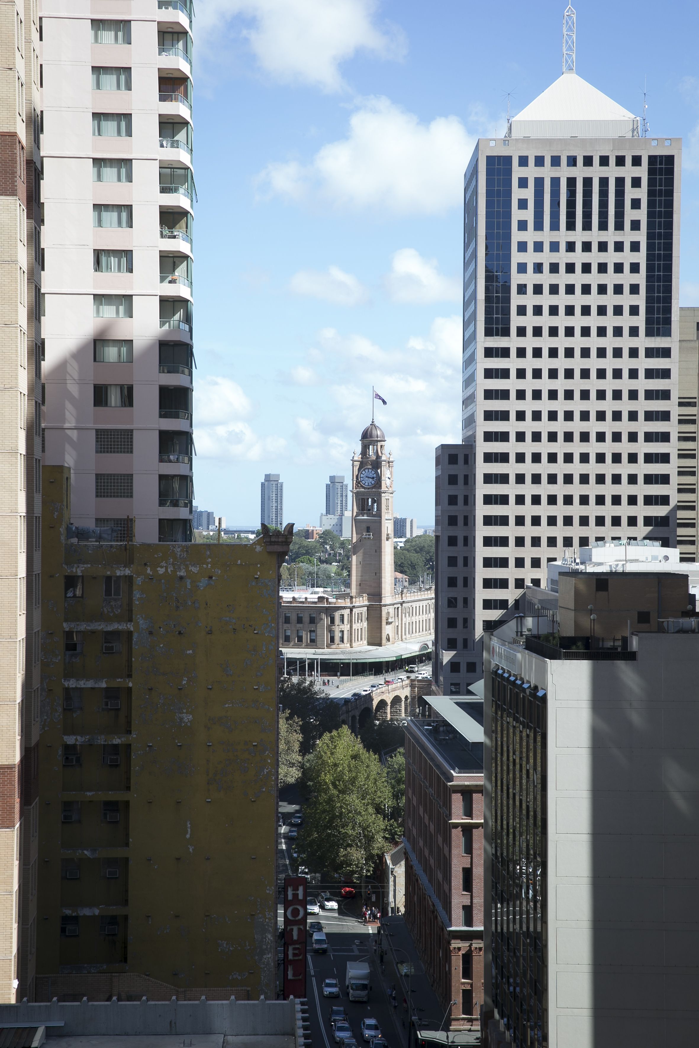 Une vue sur un paysage urbain avec un beffroi imposant, des immeubles de grande hauteur et un bâtiment jaune sur lequel on peut lire l’inscription « HÔTEL ».
