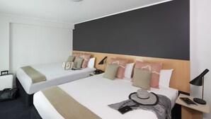 Habitación de hotel con dos camas, una mesita de noche con lámpara, una maleta y un sombrero sobre la cama.