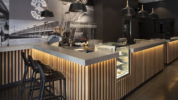 Un área de bar moderna con una barra de madera, taburetes y una exhibición de vinos.