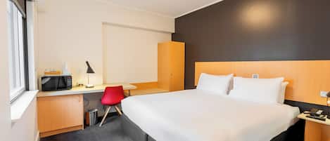 Habitación de hotel con una cama grande, un escritorio con una computadora, una silla roja y un microondas.