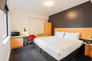 A hotel room with a large bed, a desk with a computer, a red chair, and a microwave.