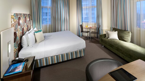 Una habitación de hotel con una cama grande, un sofá verde, una mesita y una silla.