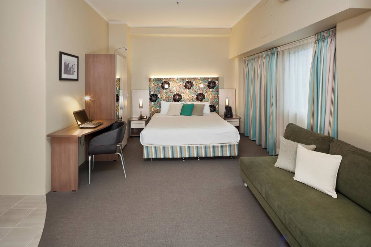 A hotel room with a bed, a desk, a green sofa, and a patterned headboard.