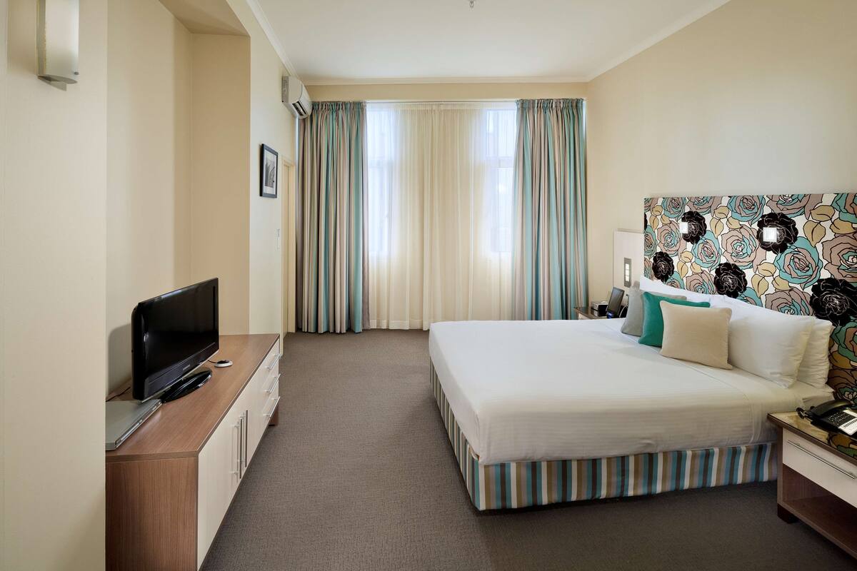 A hotel room with a bed, a TV, a desk, and a patterned headboard.