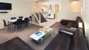 Una sala de estar moderna con una mesa de centro de vidrio, sofá de cuero y una zona de comedor con sillas y una mesa.
