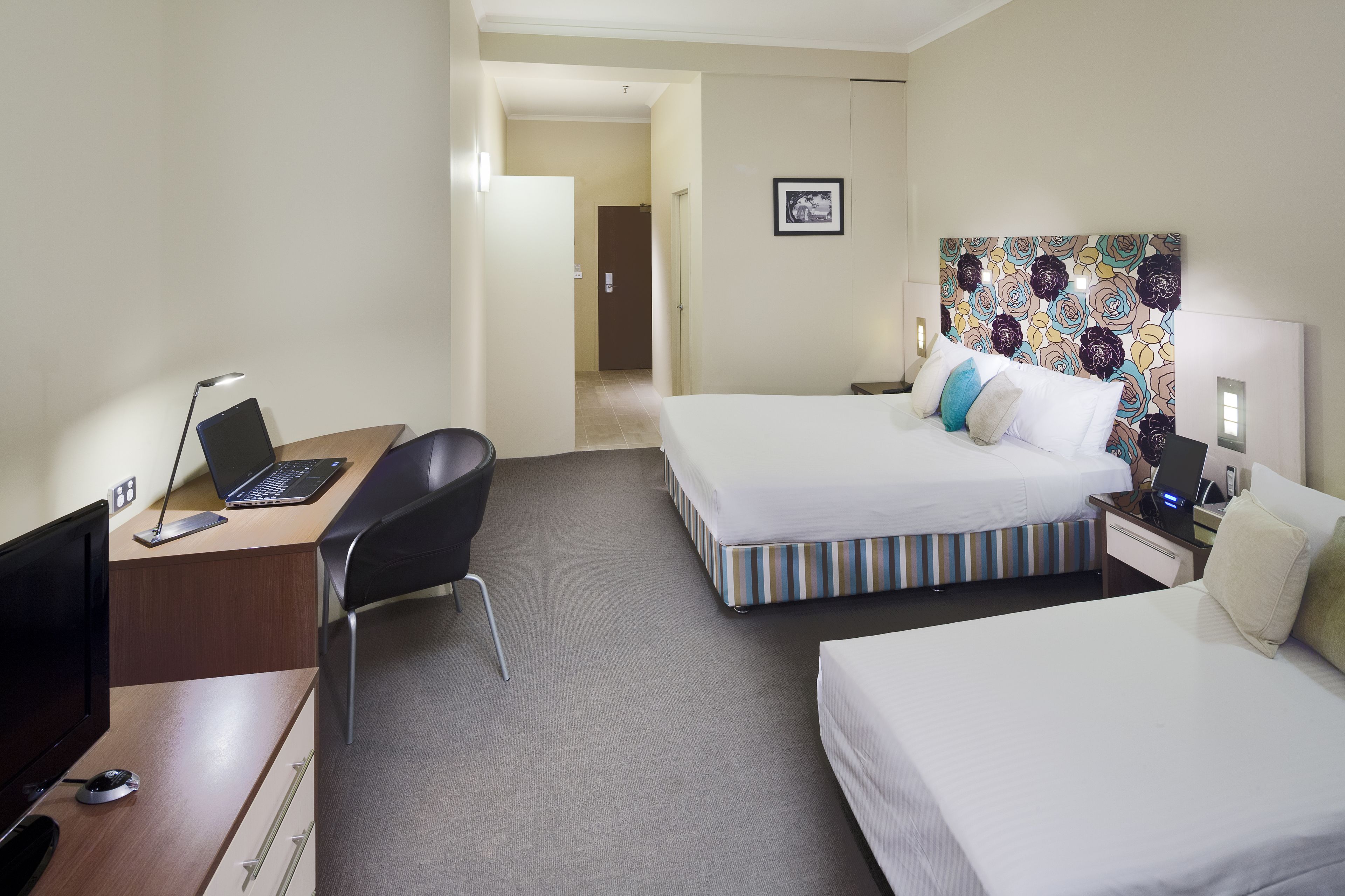 Habitación de hotel con dos camas, un escritorio con una computadora portátil, una silla y una lámpara de escritorio.