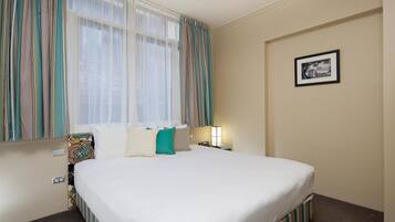 A hotel room with a large bed, a window with curtains, a bedside table with a lamp, and a framed picture on the wall.