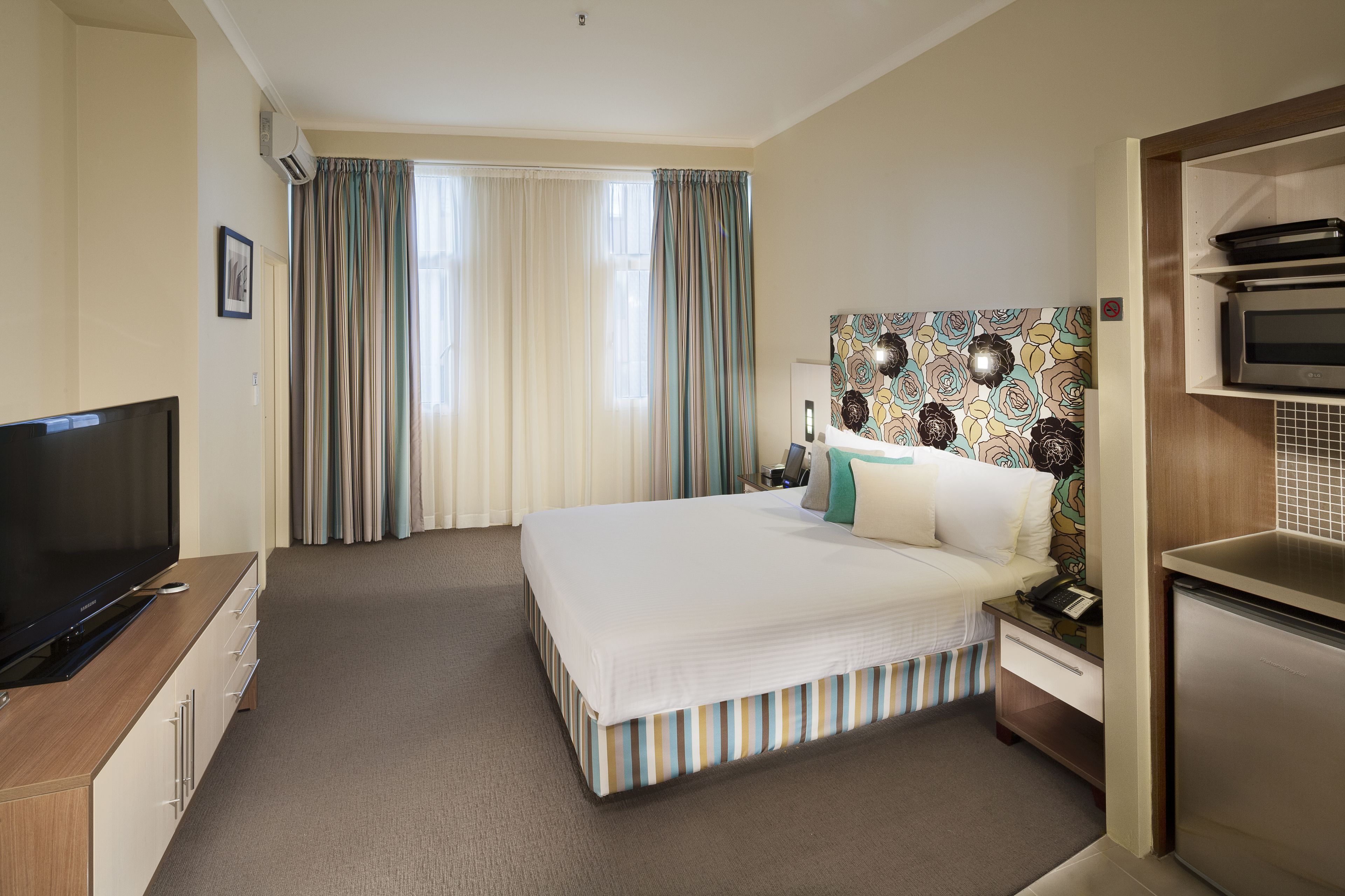 Une chambre d’hôtel équipée d’un lit, d’une télévision, d’un bureau avec un téléphone et d’une kitchenette.
