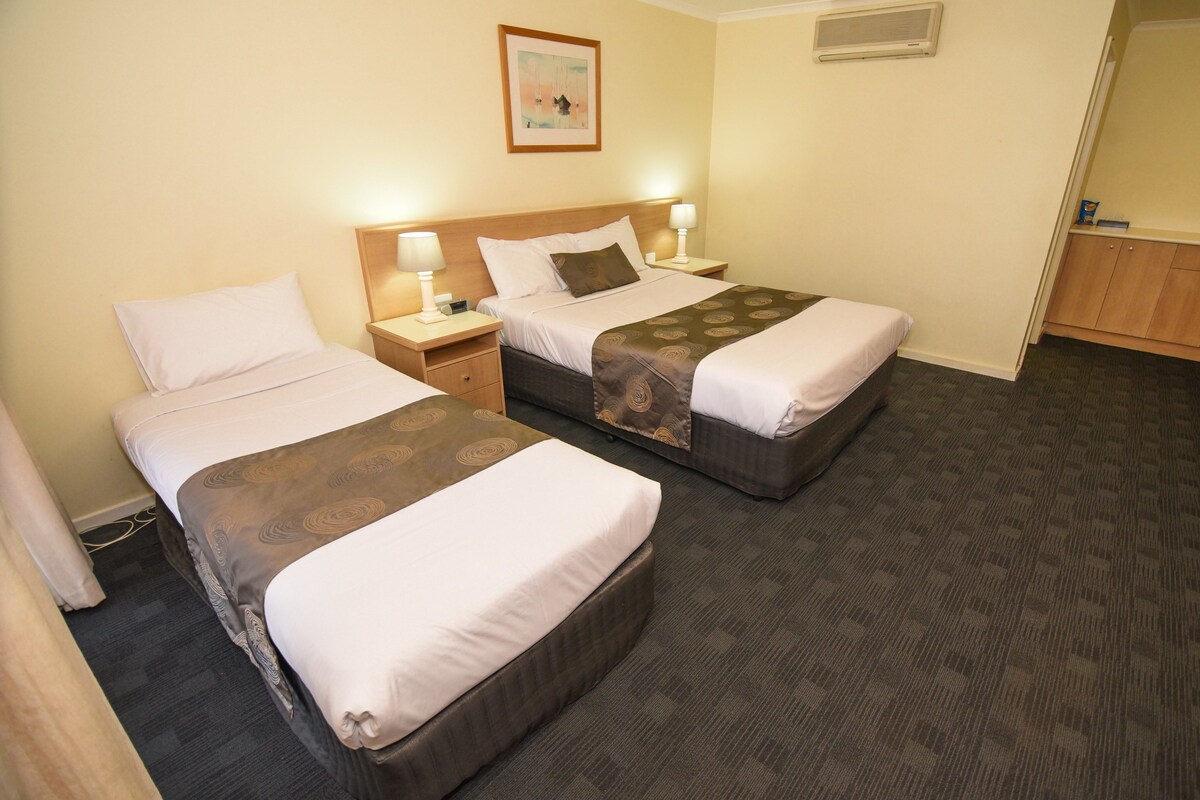 Habitación de hotel con dos camas, una mesita de noche con lámparas, un cuadro en la pared y piso alfombrado.