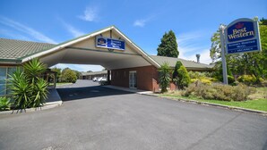 Ein Best Western Sandown Heritage Motel mit überdachter Einfahrt, einem Ziegelgebäude und blauem Himmel.