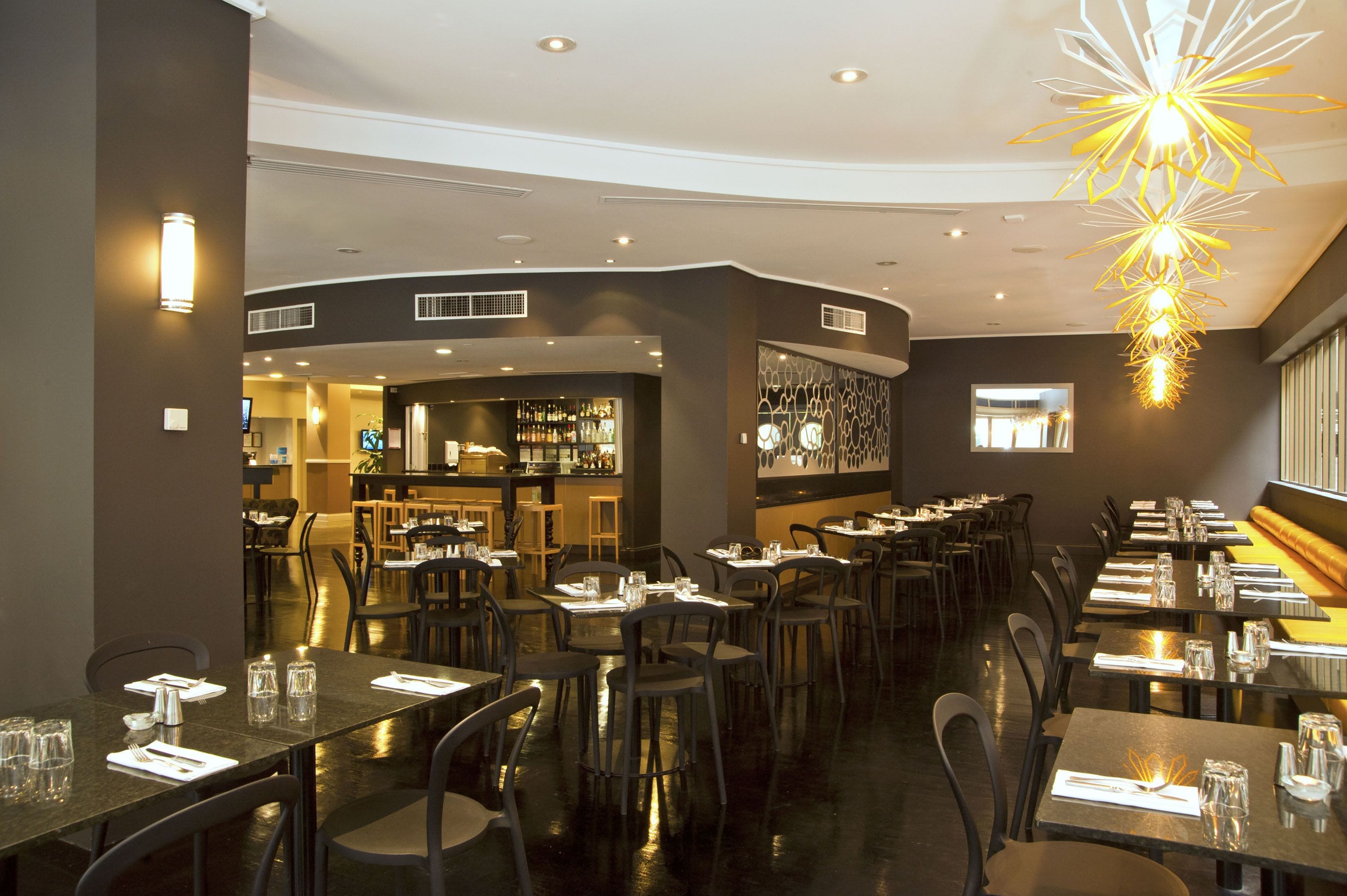 Un restaurant doté de nombreuses tables et chaises, d’un bar et d’un lustre moderne.