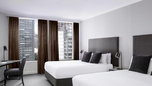 Une chambre d’hôtel avec deux lits, un bureau, une chaise et une vue sur des immeubles de grande hauteur.