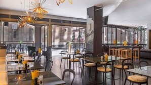 Un intérieur de restaurant moderne, caractérisé par de hauts plafonds, des luminaires aux formes géométriques et une variété d’aménagements, notamment des tables et des chaises.