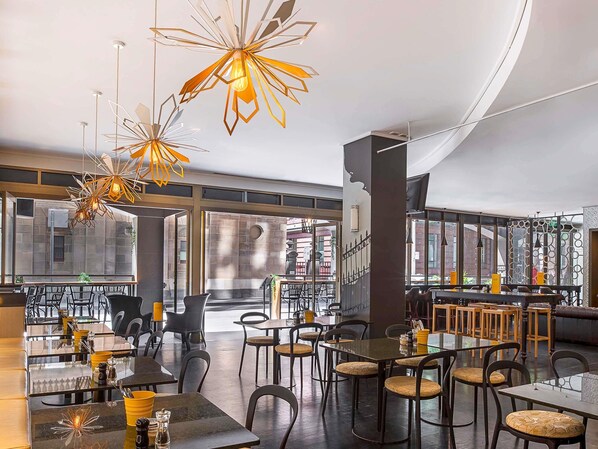 A modern restaurant interior with high ceilings, geometric light fixtures, and a mix of seating arrangements including tables and chairs. - Mantra on Little Bourke Melbourne (Melbourne)