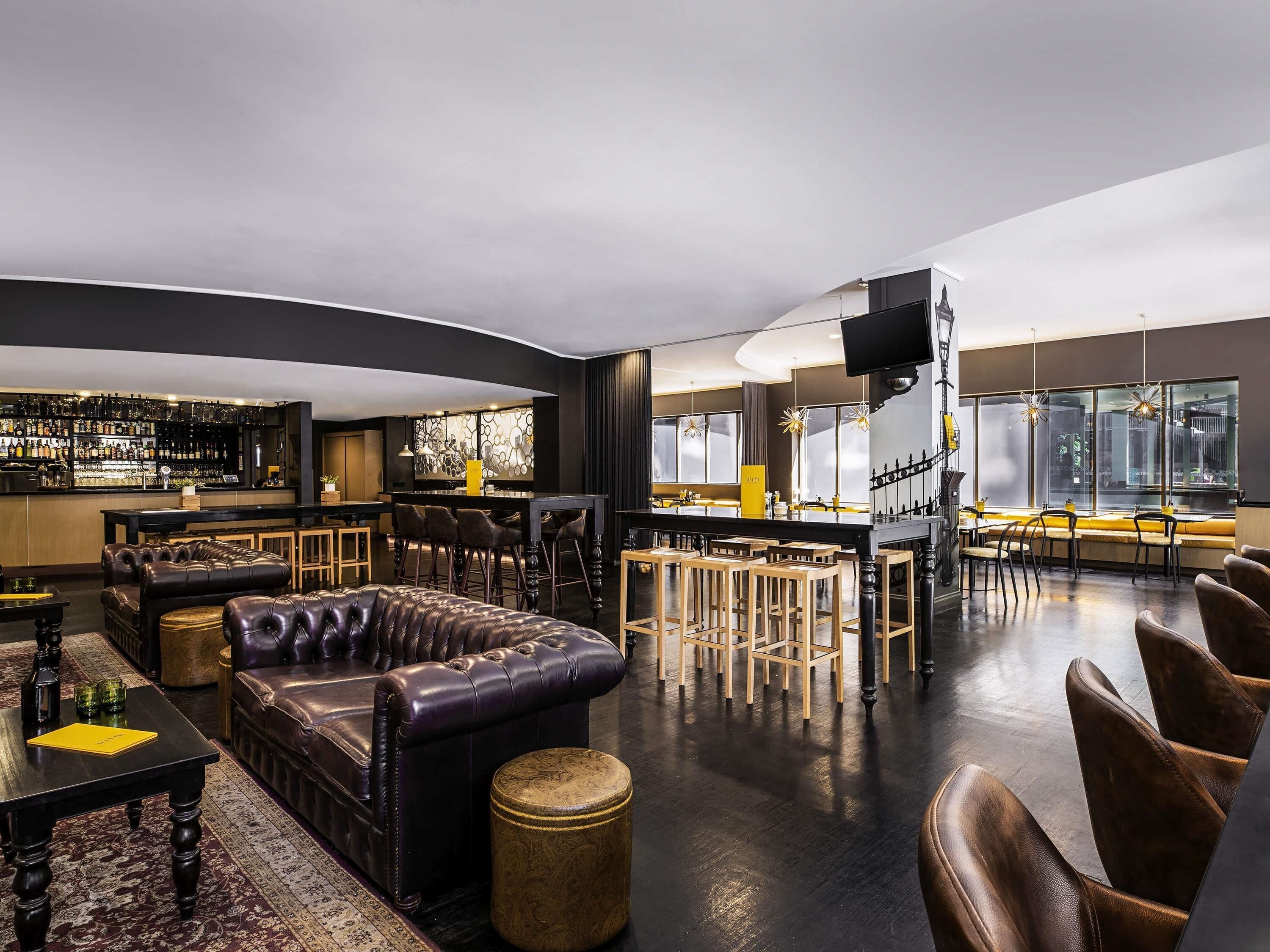 A modern bar area with leather seating, a bar counter, and a kitchen in the background.