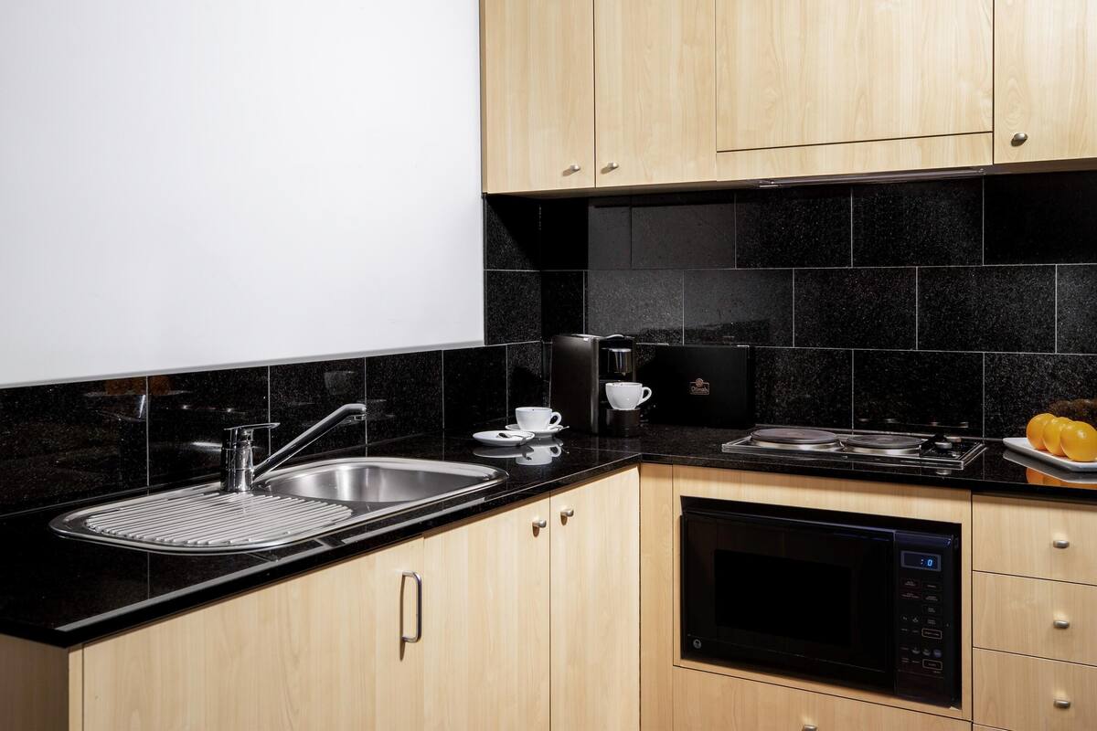 A modern kitchen with a black countertop, stainless steel sink, and a built-in microwave.