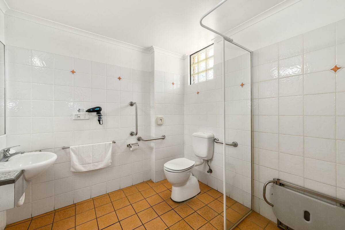 A bathroom with white tiled walls, a white toilet, a sink, and a shower area.