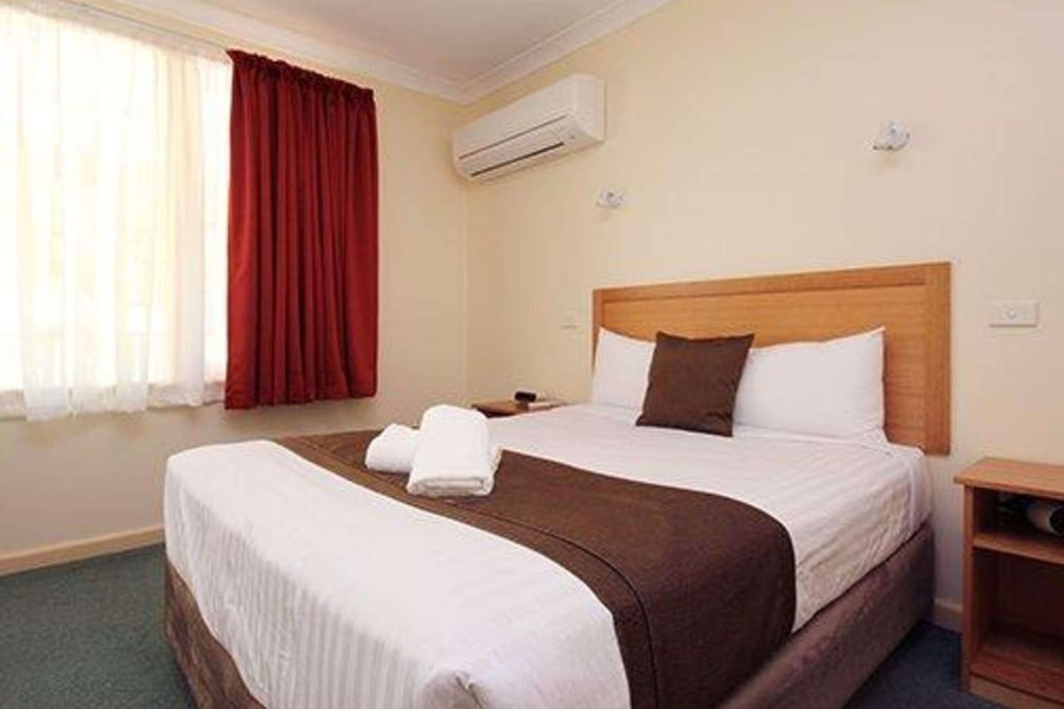 Una habitación de hotel con cama, mesita de noche, aire acondicionado y ventana con cortinas.