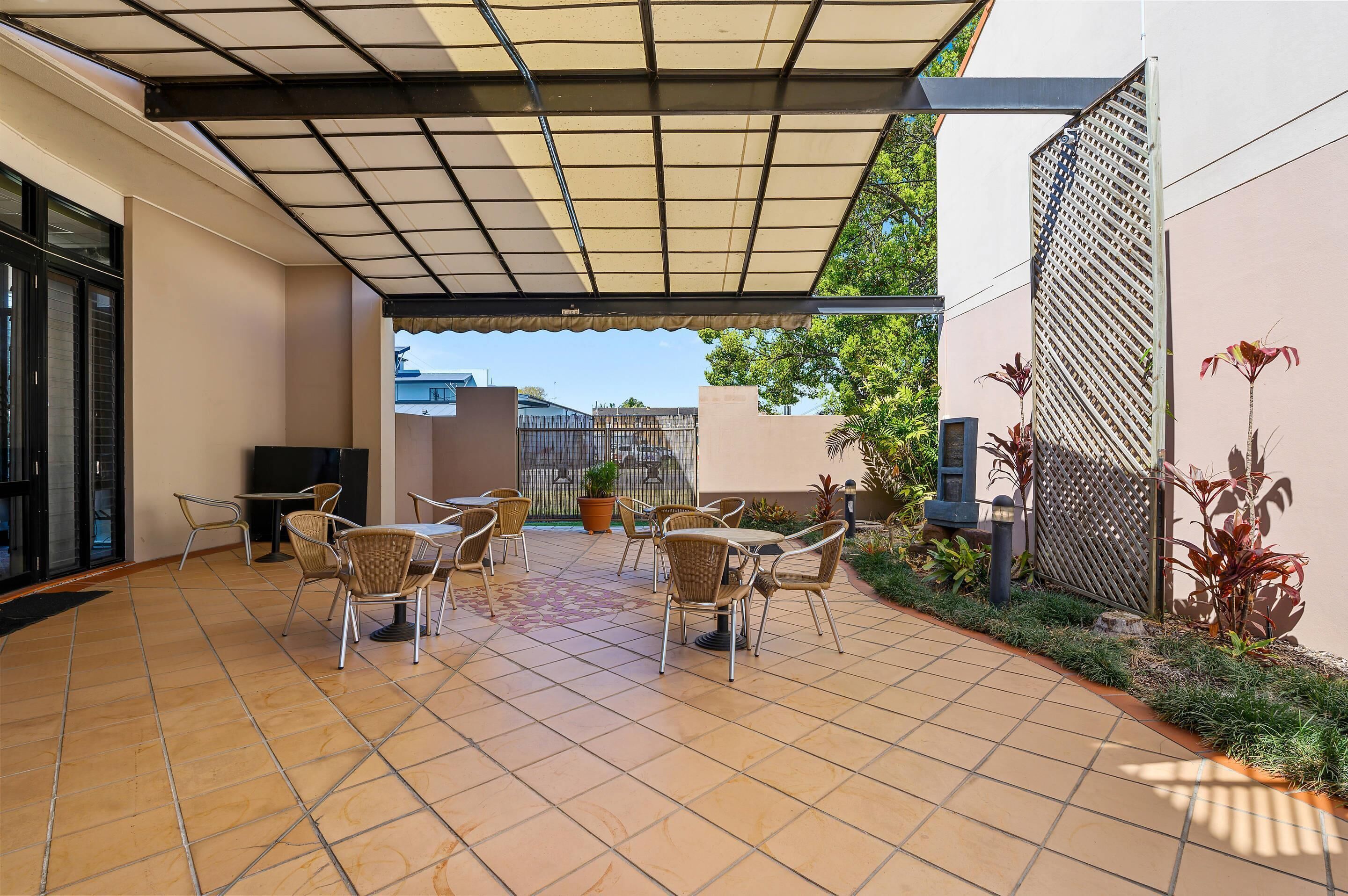 A covered patio area with tiled flooring, outdoor seating, and potted plants.