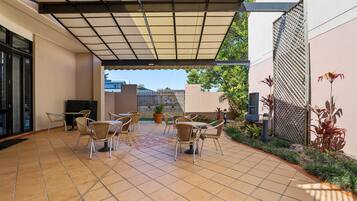 A covered patio area with tiled flooring, outdoor seating, and potted plants.
