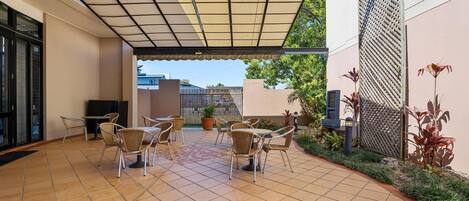 A covered patio area with tiled flooring, outdoor seating, and potted plants.