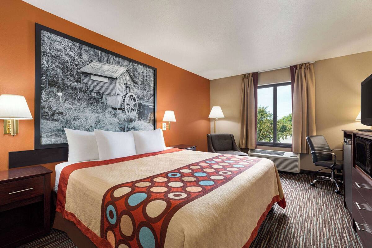 Une chambre d’hôtel avec un grand lit, deux lampes de chevet, un bureau, une chaise, une télévision et une fenêtre avec des rideaux.