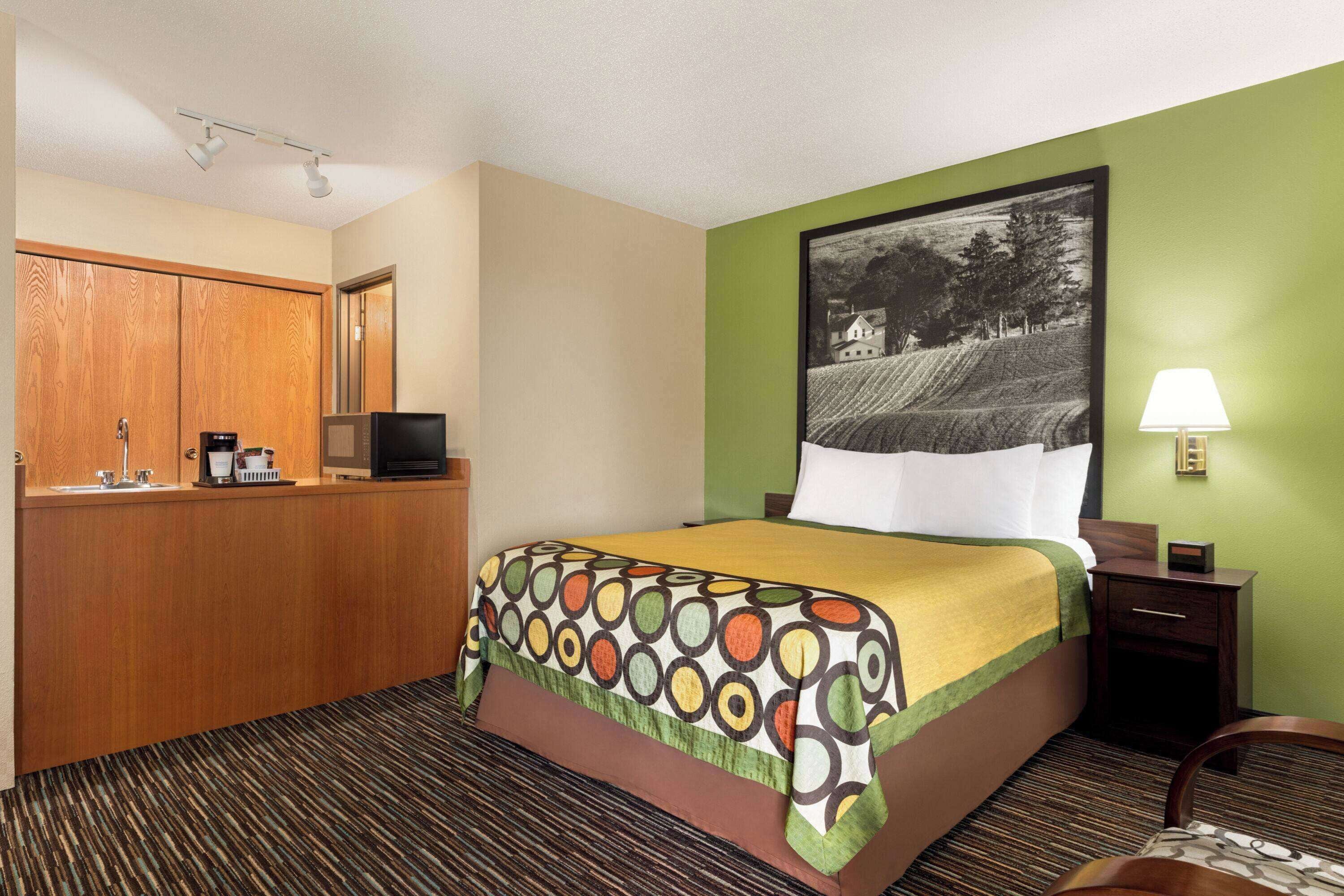 A hotel room with a bed, a desk with a television, a lamp, and a picture on the wall.