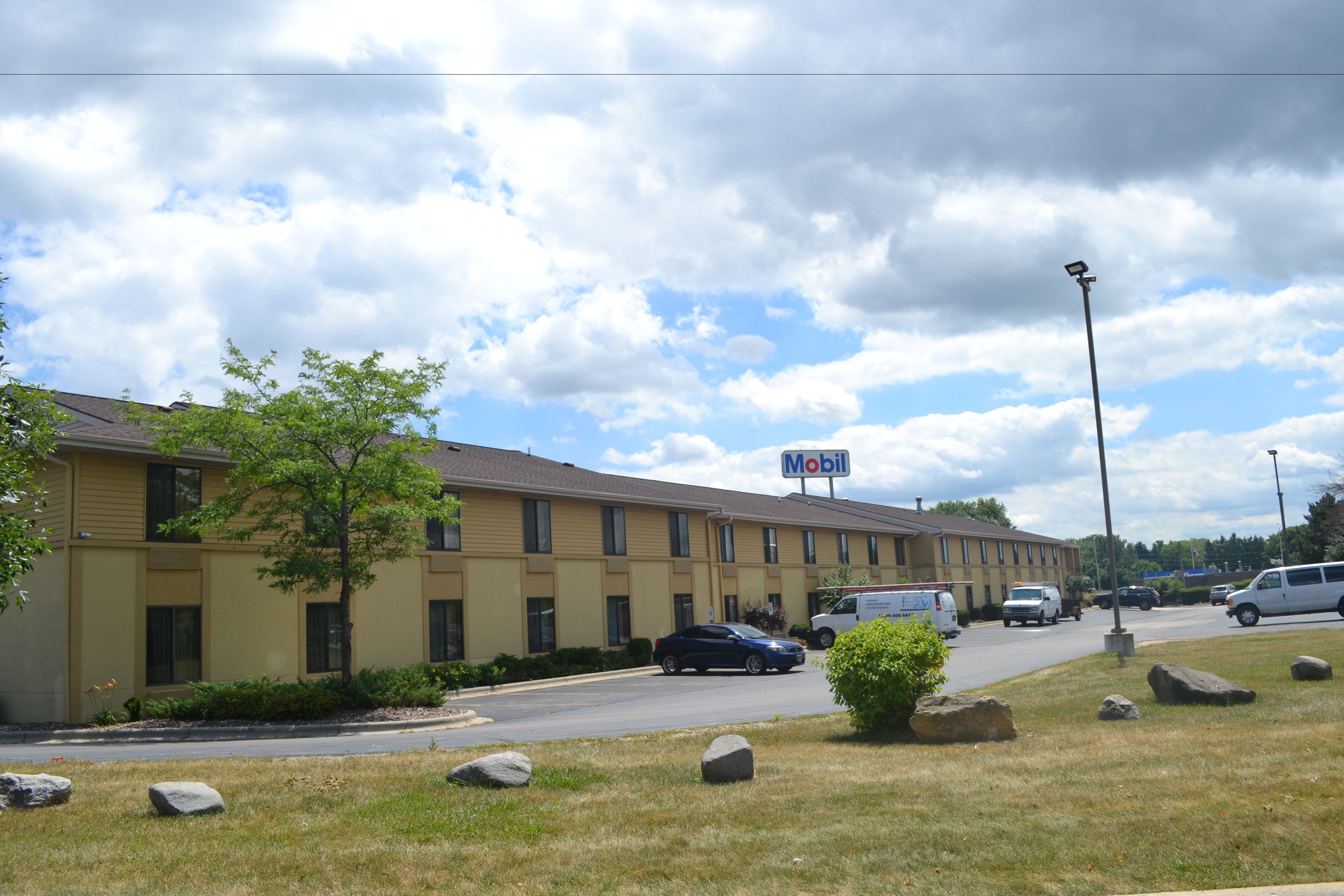A Mobil-branded motel with multiple rooms, a parking lot, and a grassy area with rocks.