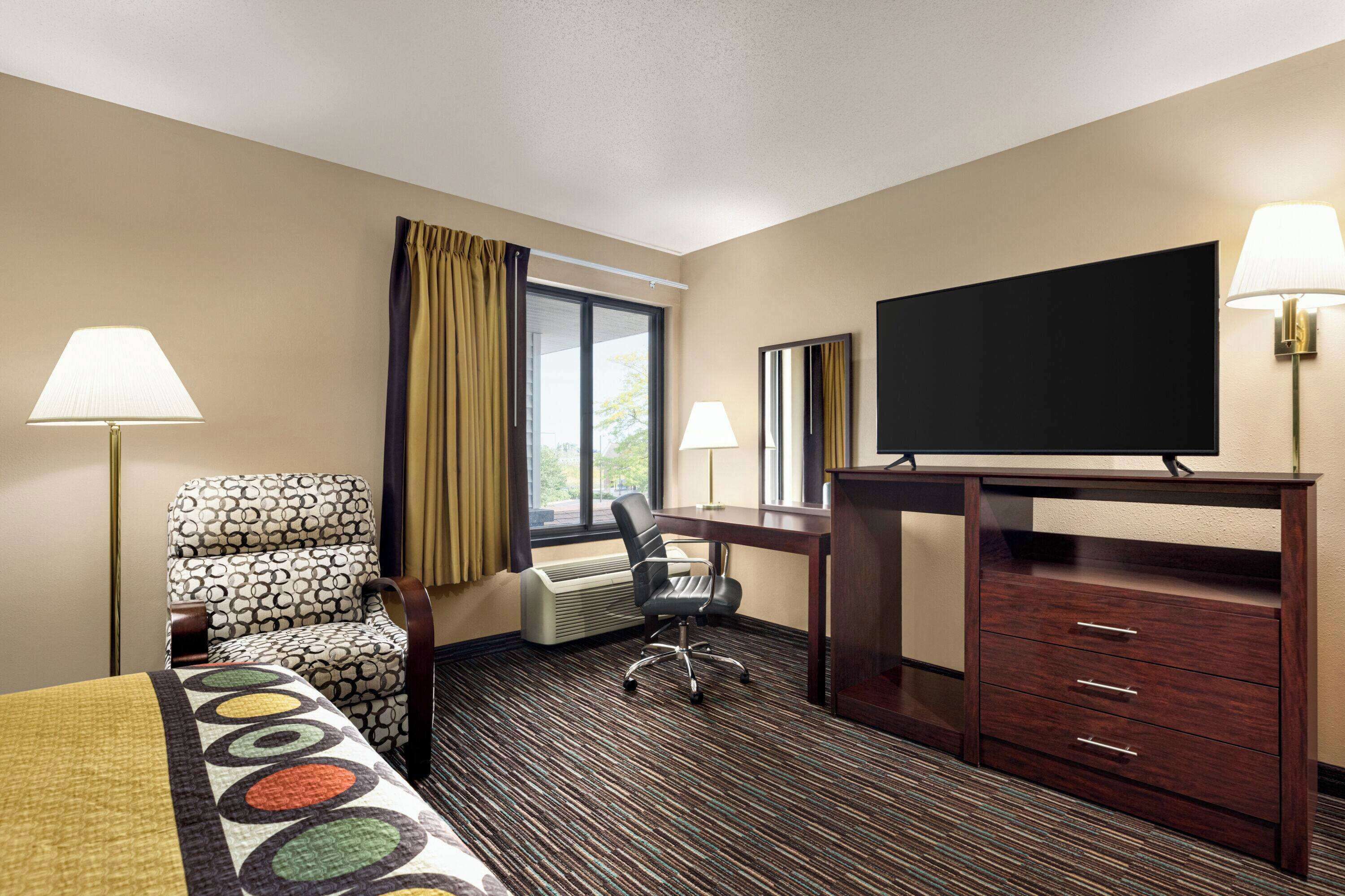 A hotel room with a bed, a desk, a chair, a TV, and a dresser.