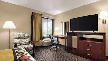 A hotel room with a bed, a desk, a chair, a TV, and a dresser.