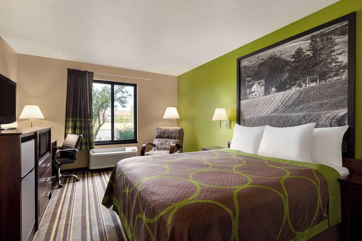 Une chambre d’hôtel avec un grand lit, deux chaises, un bureau et une fenêtre avec des rideaux.