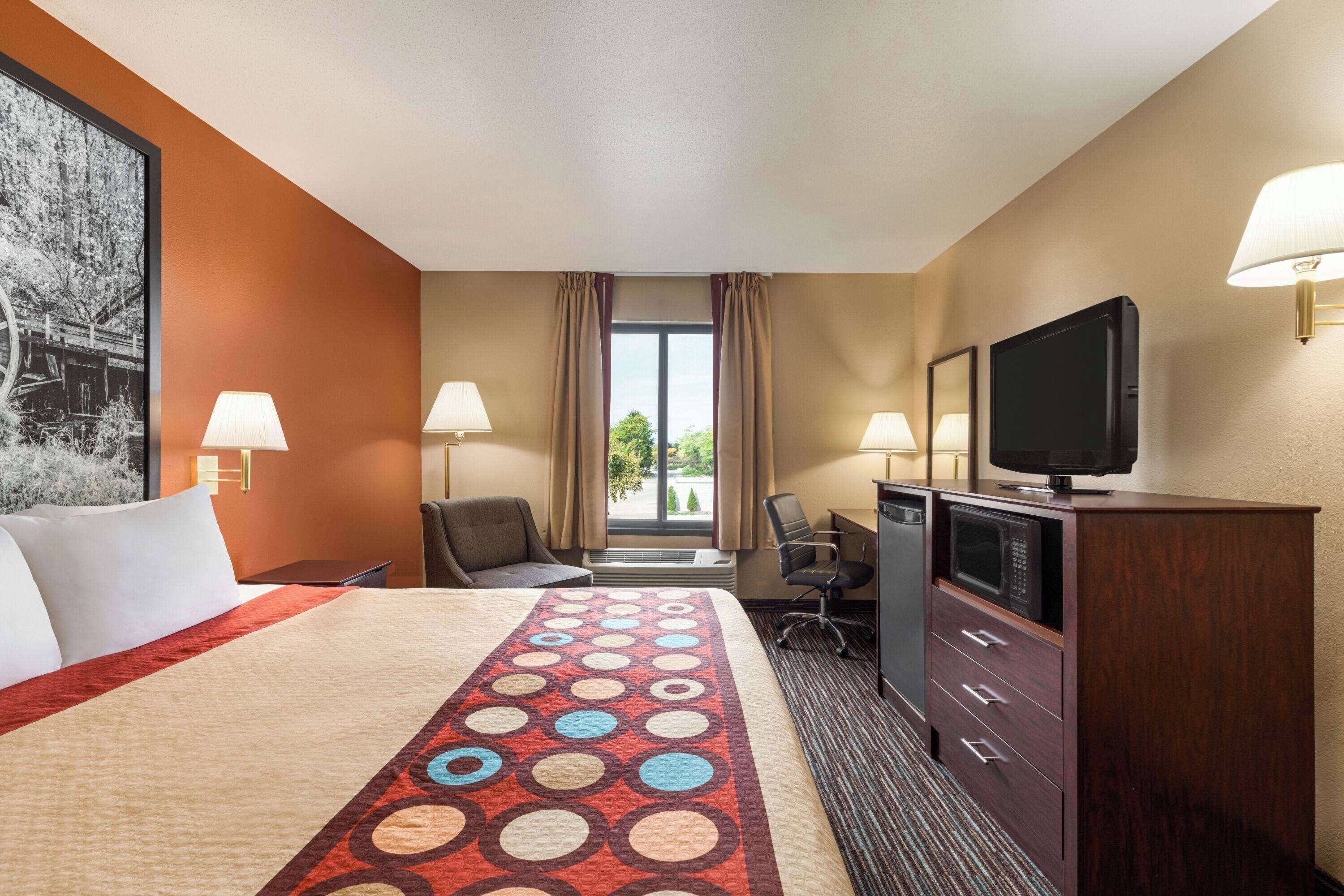 A hotel room with a large bed, a desk with a television, a chair, and a dresser.