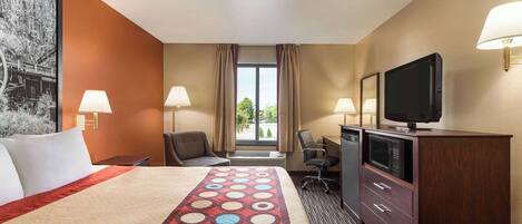 A hotel room with a large bed, a desk with a television, a chair, and a dresser.