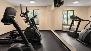 Un gimnasio con cintas de correr y bicicletas estáticas, ventanas amplias y un espejo grande.