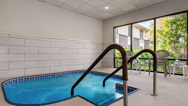 Una piscina interior con agua cristalina y azul, rodeada por un muro de azulejos y un ventanal que da al exterior.