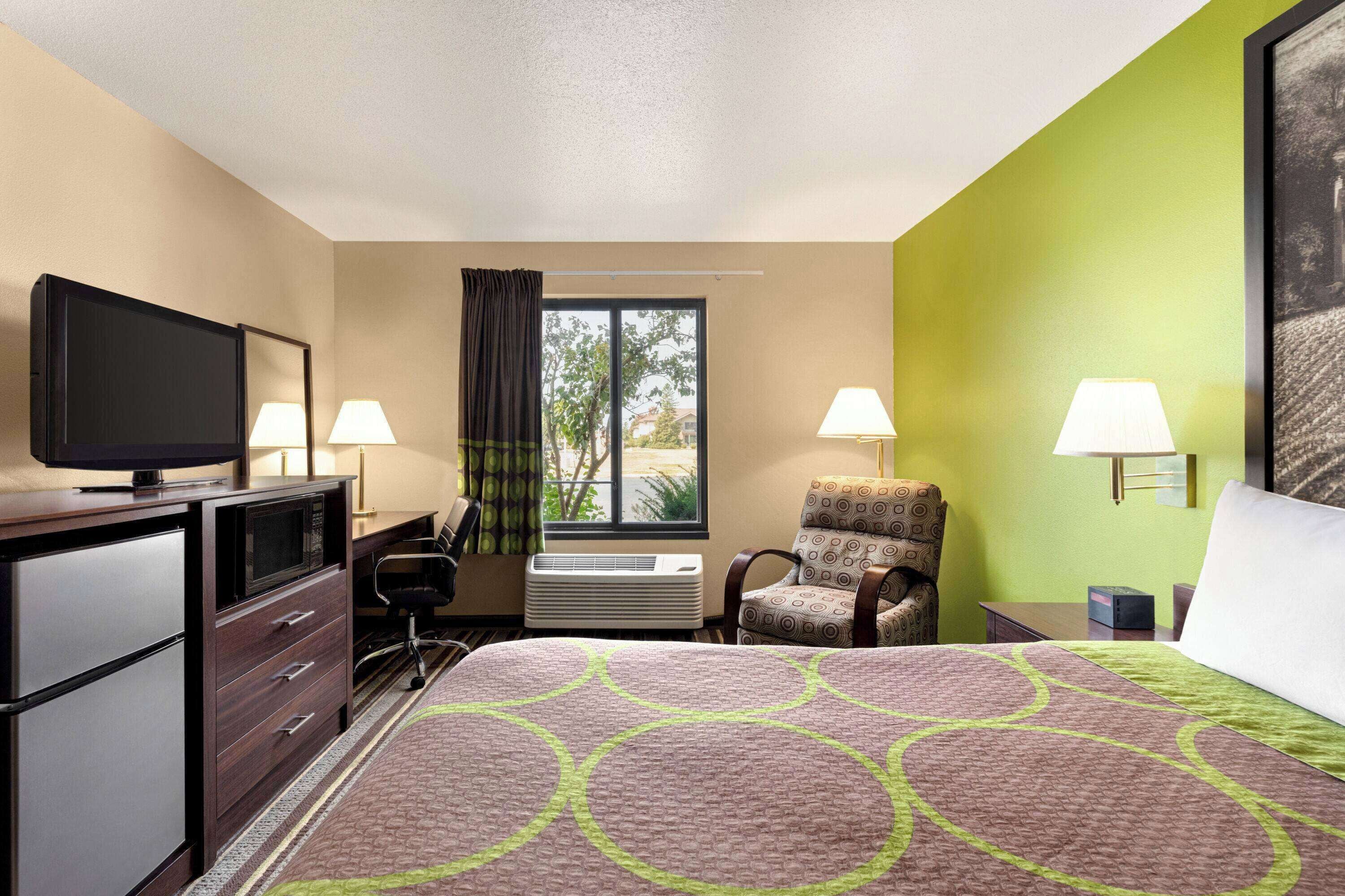 A hotel room with a bed, a desk with a television, a chair, two lamps, and a window with curtains.