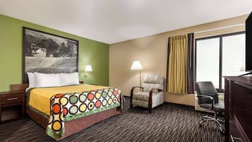 Quarto de hotel com cama, duas cadeiras, escrivaninha, luminária e uma janela grande com cortinas.