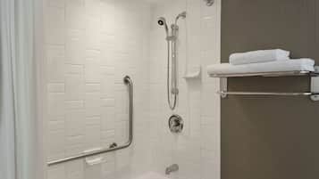 A modern bathroom with white subway tile walls, a white bathtub, a shower with a handheld showerhead, and a towel rack with folded towels.