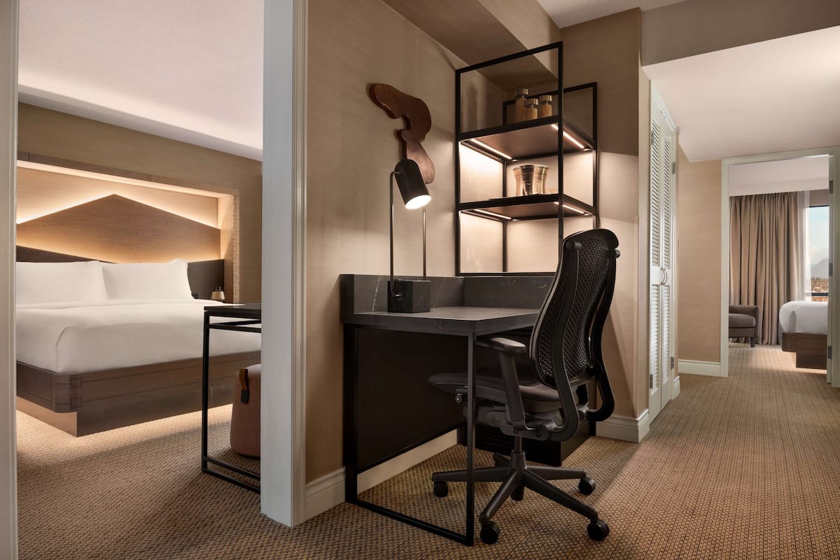 A hotel room with a bed, desk, chair, and built-in shelving unit.