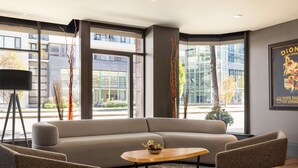 A modern hotel lobby with a large sofa, two armchairs, a coffee table, and a floor lamp. Large windows offer views of the city. - Hilton Vancouver Airport (Richmond)