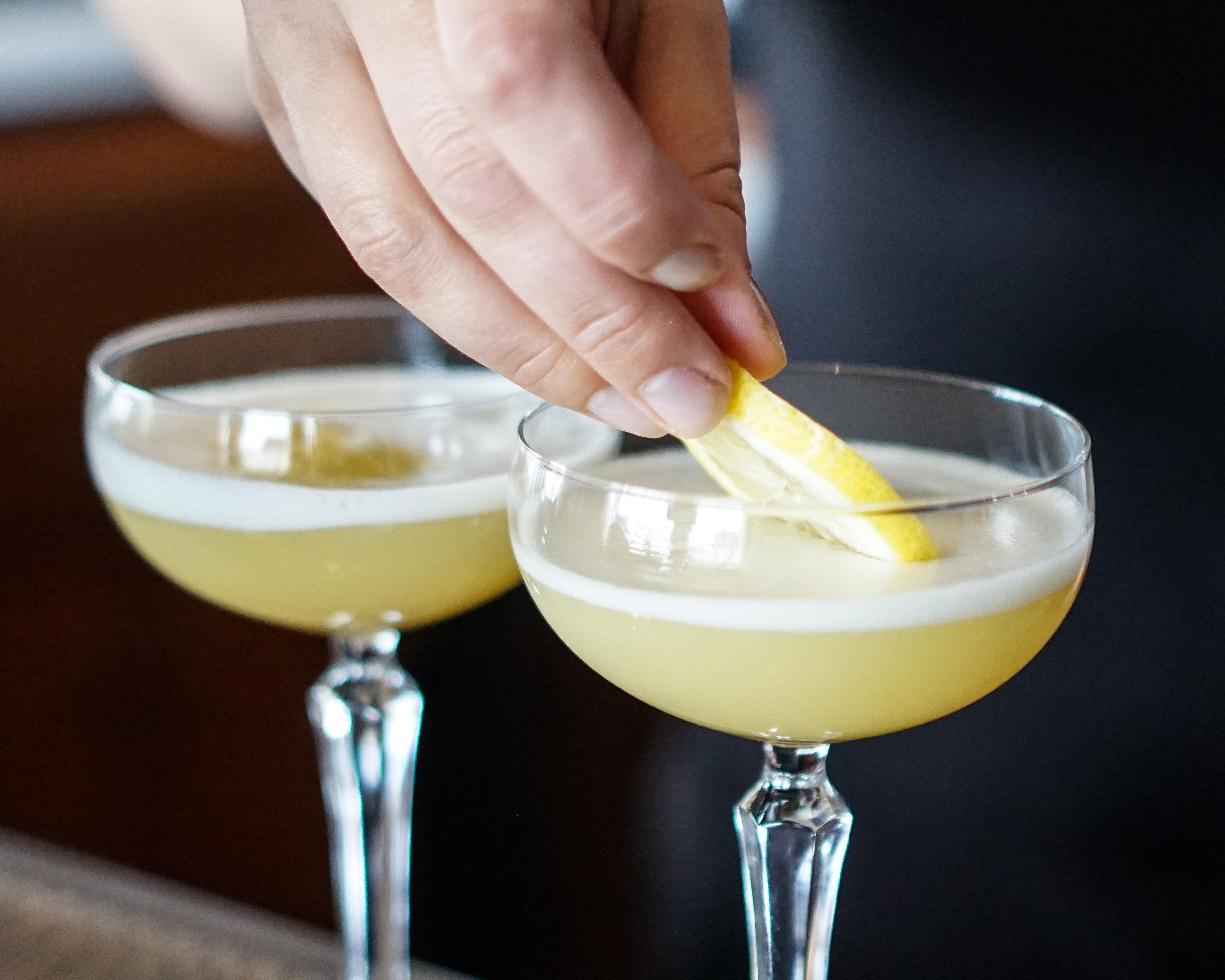 A hand squeezing a lemon into a cocktail glass.